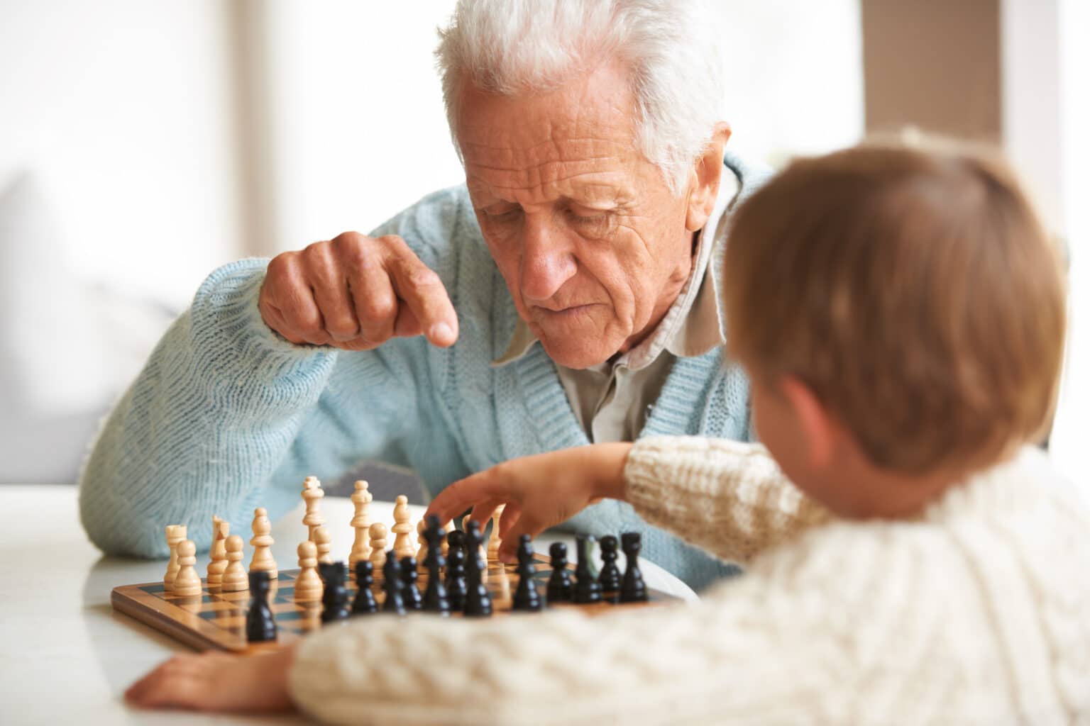 A grandfather teaching his grandson how to play chess